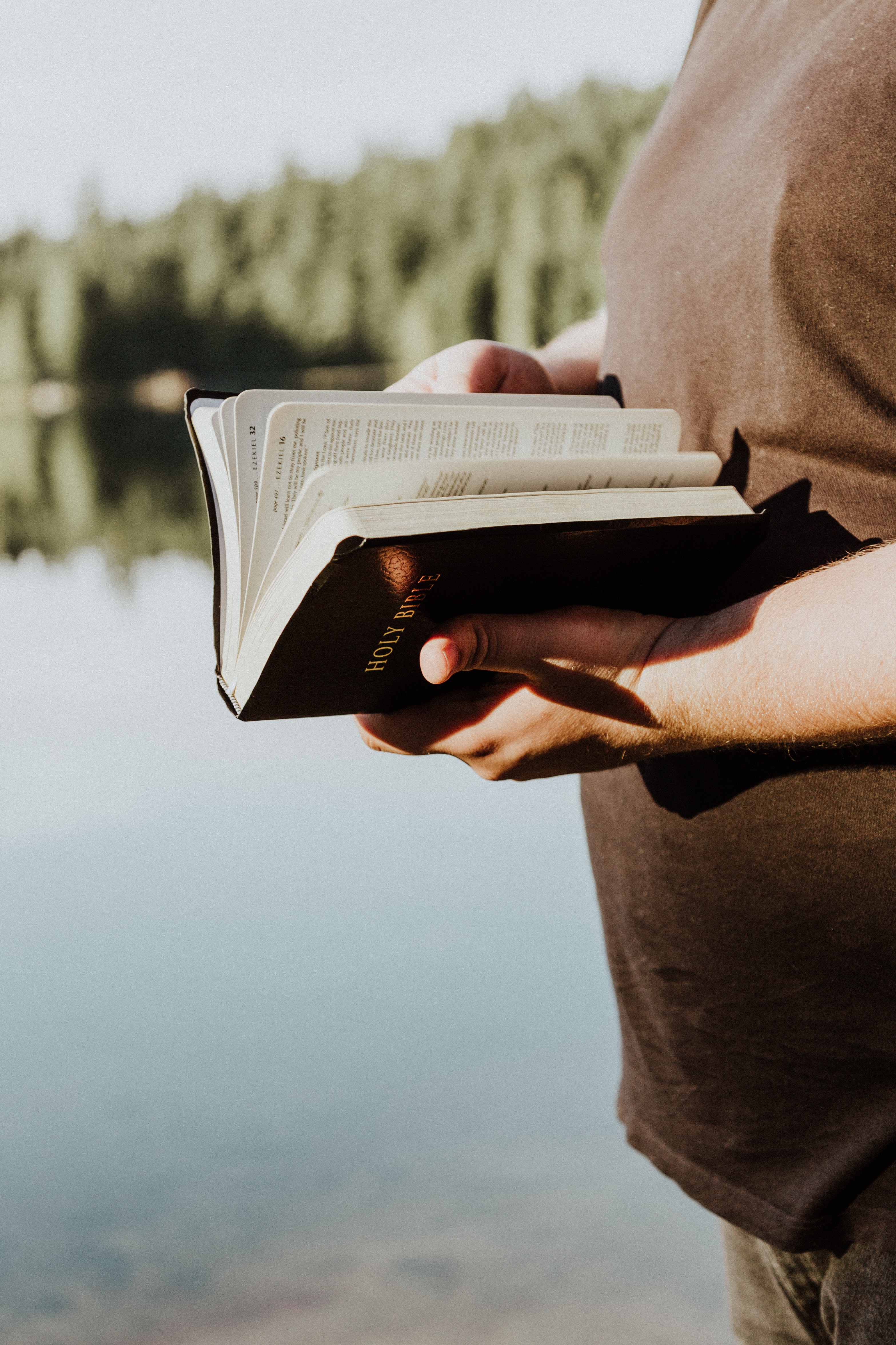 man holding a bible on the lake 